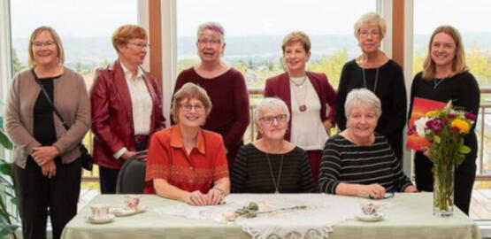 nine women posing for a photo at a long table