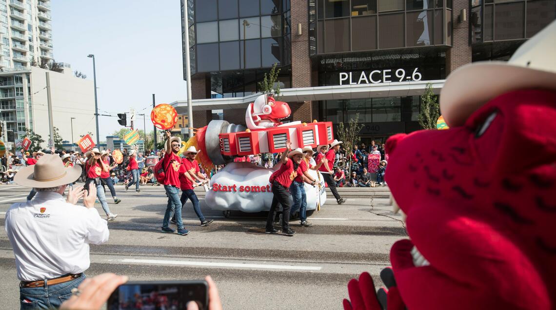 The parade featuring the UCalgary's float of Rex on a spaceship with the real Rex in the forefront of the image. 