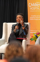 A woman sits on a stage holding a microphone