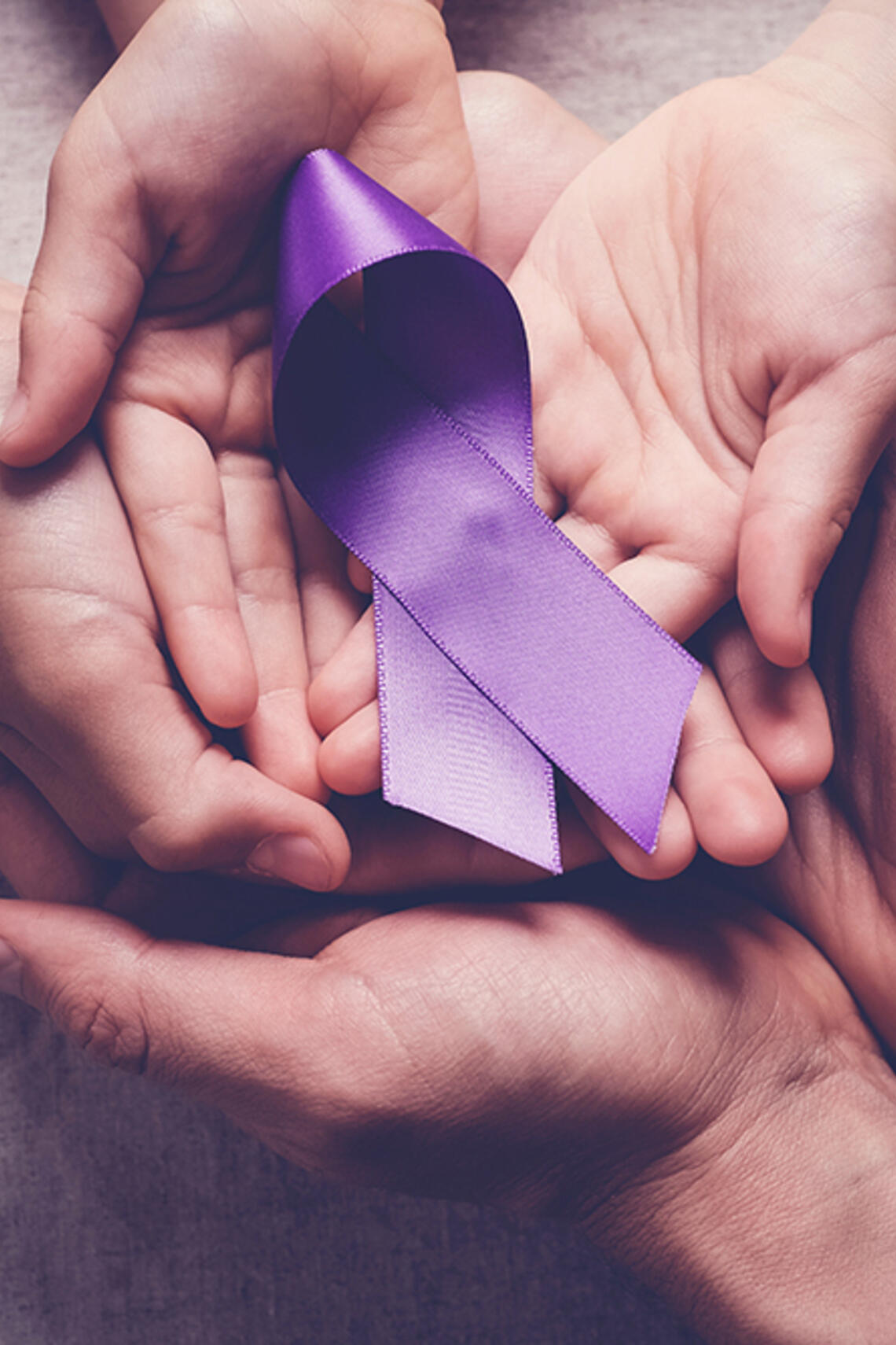 adults' hands and child's hands cradling a purple ribbon