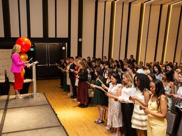 Speaker on stage at Pinning Ceremony as students read nursing pledge.