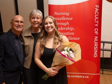 Student and family pose in front of nursing banner. 