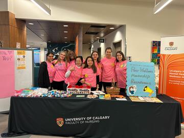 group of nursing students in pink shirts standing in front of an information table