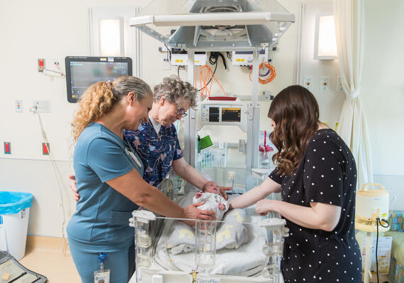 nurses and parent around babie in NICU