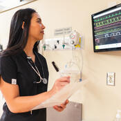 Nurse in scrubs looking at monitor of vital stats